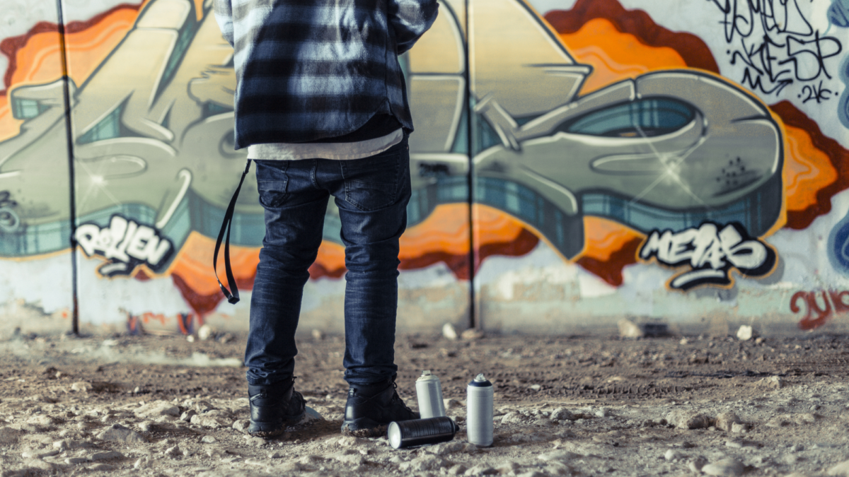 Low section view artist standing near spray can front graffiti wall